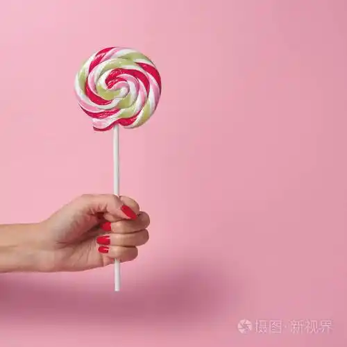 女人手拿着五颜六色的旋转棒棒糖在粉红色的背景上夏季最小概念