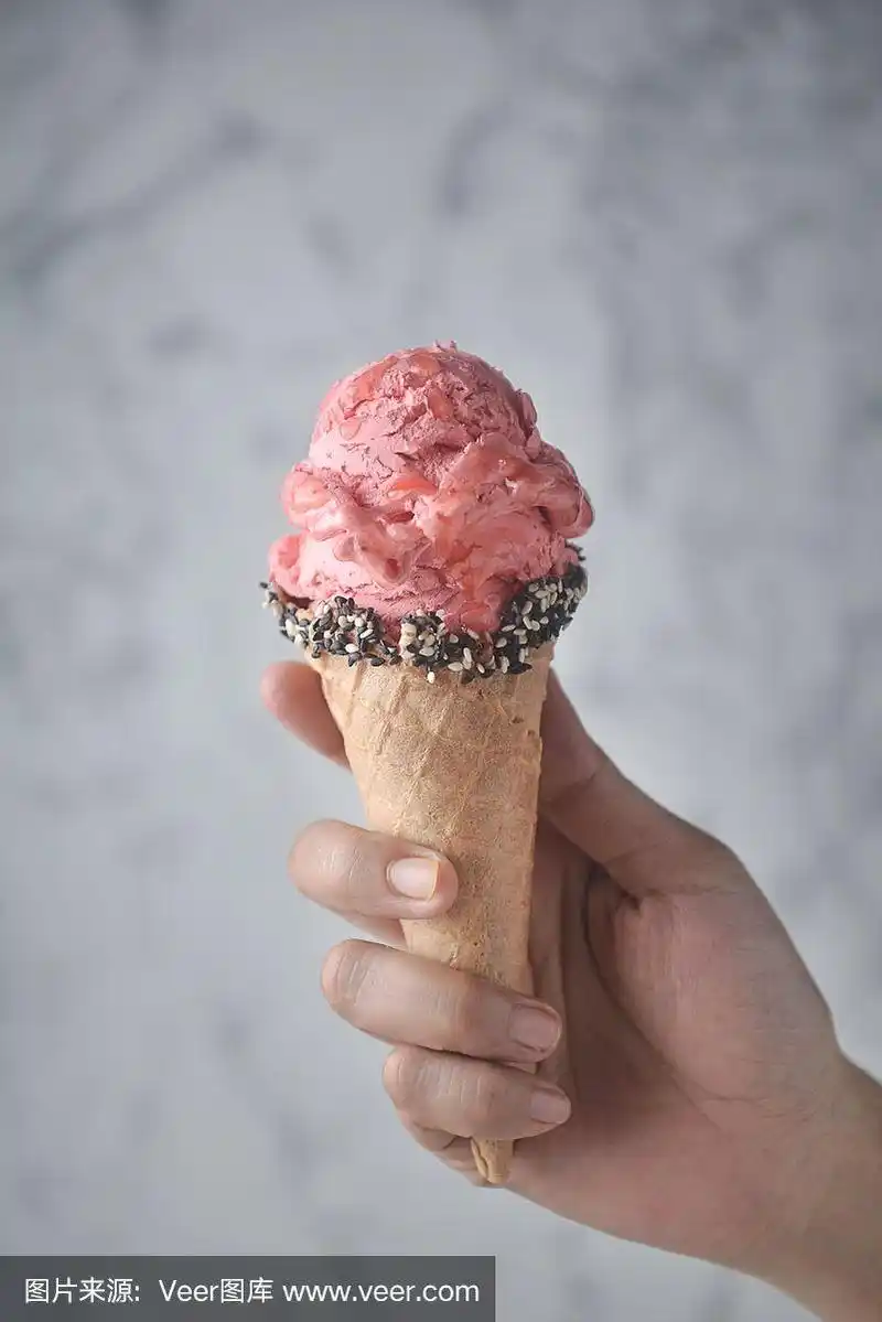 女人手拿着草莓冰淇淋和装饰有白芝麻和黑芝麻的华夫蛋筒.
