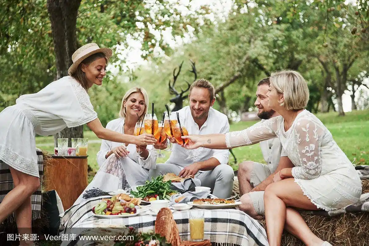 团结亲密的人.朋友们坐在草地上,喝着新鲜的鸡尾酒