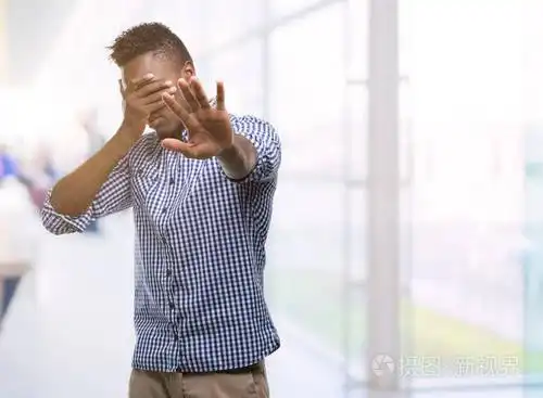 年轻的非洲裔美国人穿着蓝色衬衫, 用手捂着眼睛, 用悲伤和恐惧的表情