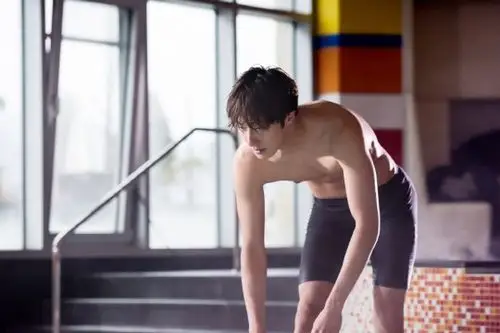 身穿泳衣,正在做着拉伸动作,展现出如游泳运动员般完美的肌肉身材