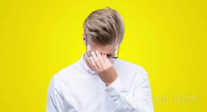年轻英俊的金发男人疲倦地揉鼻子和眼睛感到疲倦和头疼.
