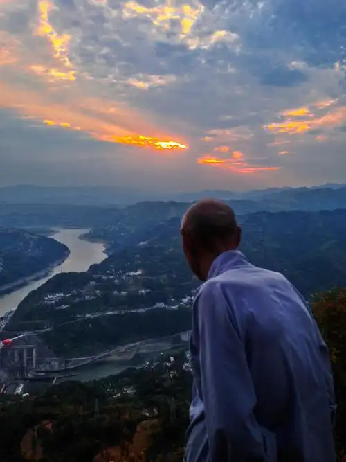 照片描述一位老人,站在高出看着西下的夕阳和美丽的风景,在想思考着