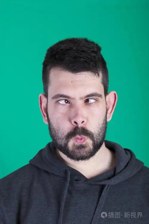 深色头发的男人眯着眼睛在绿色背景的工作室里摆姿势