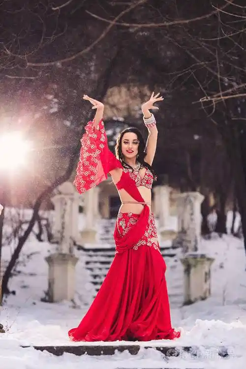 美丽的年轻女孩跳舞肚皮舞在冬季在雪上的公园红色礼服