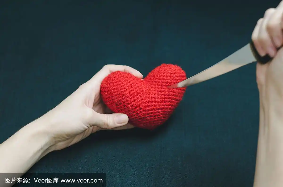 一个年轻女孩的手拿着一颗红心和一把刀在黑色的背景.神秘的照片