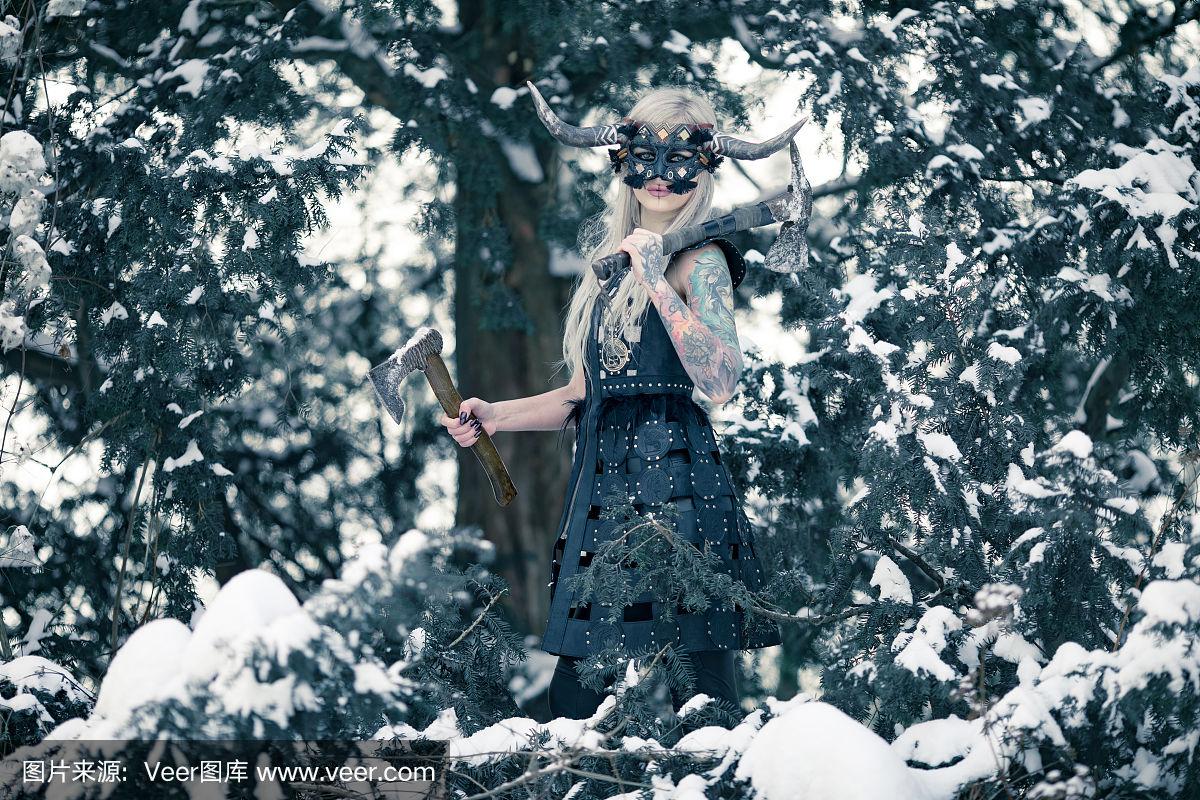 美丽的女战士在北欧海盗的形象与角面具头盔和两把斧头在冬天的雪林.